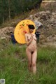 A naked woman holding an orange umbrella in a field.