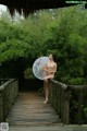 A naked woman holding an umbrella standing on a wooden bridge.