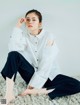 A woman sitting on a white rug wearing a white shirt and black pants.