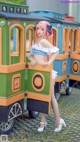 A woman with pink hair standing in front of a train.