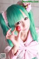 A woman with green hair holding a strawberry in her hand.