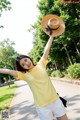 A woman in a yellow shirt and white shorts holding a straw hat.