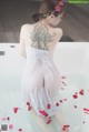A woman in a white dress sitting in a bathtub with rose petals.