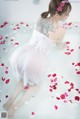 A woman in a white dress sitting in a bathtub filled with rose petals.