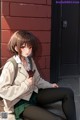 A girl sitting on the ground in front of a brick wall.