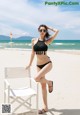 A woman in a black bikini sitting on a white chair on the beach.