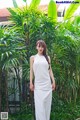 A woman in a white dress standing in front of a palm tree.