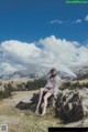 A woman sitting on top of a rock holding an umbrella.