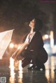 A woman crouching down in the rain holding an umbrella.