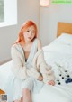 A woman sitting on a bed wearing a white sweater.